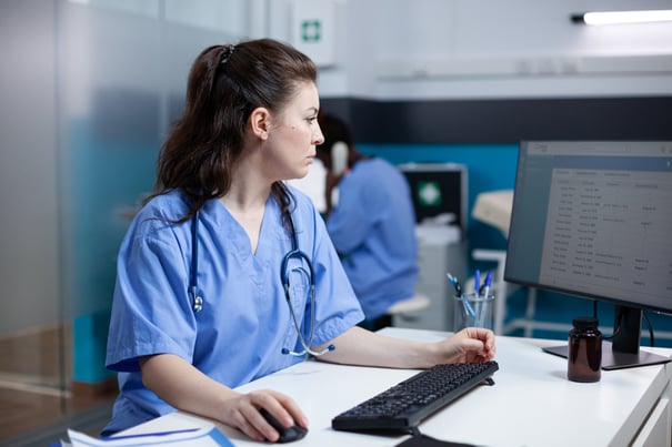 caucasian-nurse-checking-appointments-list-computer-monitor-sitting-clinic-desk-focused-adult-woman-healthcare-expert-working-medical-office-with-stethoscope-around-neck