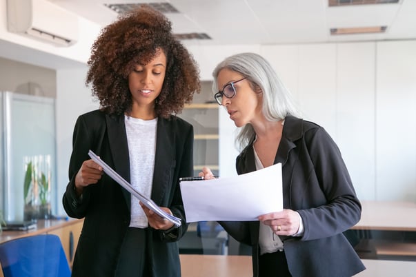 content-young-manager-showing-document-adult-colleague-two-pretty-content-female-colleagues-holding-papers-standing-office-room-teamwork-business-management-concept